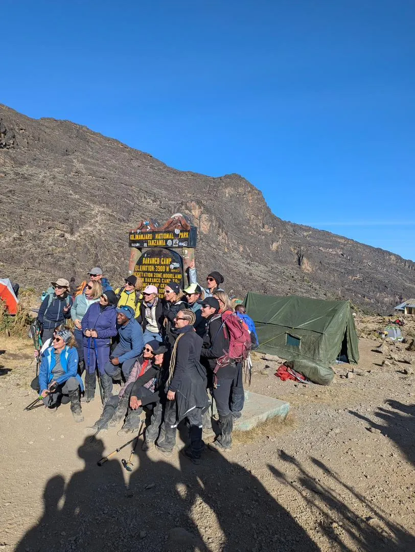 A trekking group gathered at the Barranco Camp sign below the mountain