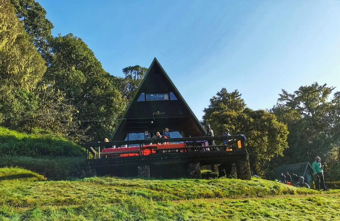 A wooden A-frame hut among the trees on the forested lower slopes