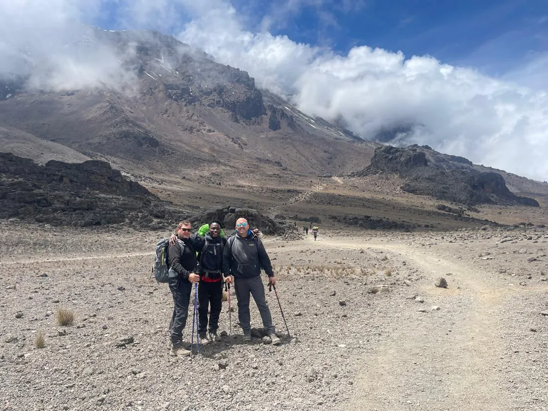 Three trekkers on the trail across the saddle with Kibo peak behind