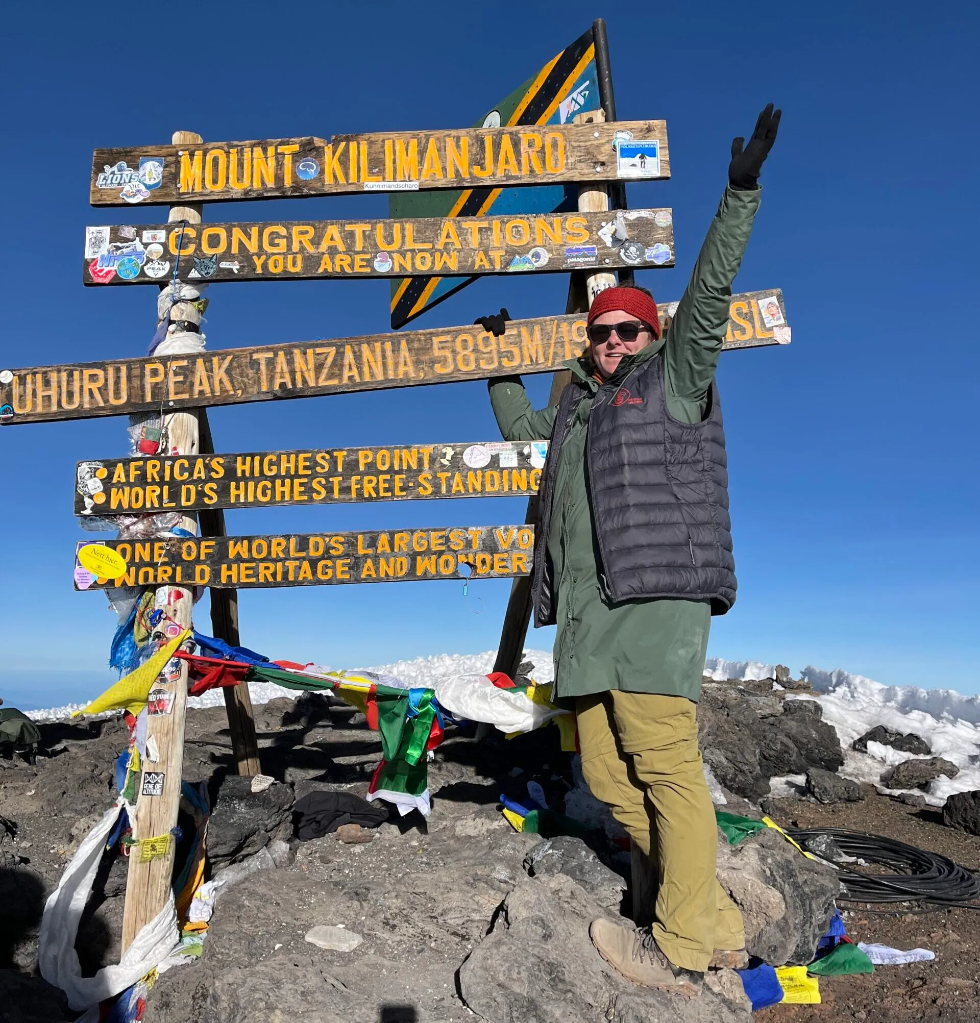 A climber celebrating at the Uhuru Peak summit sign