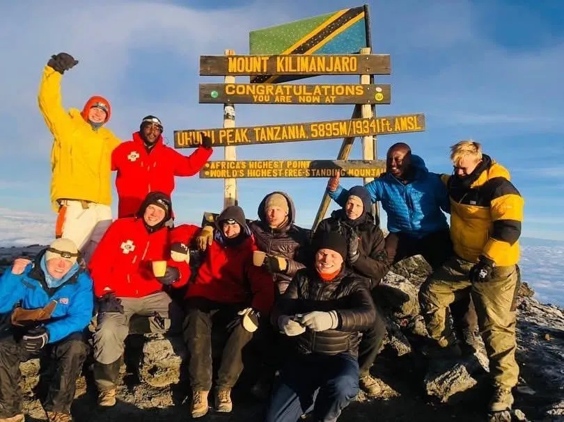 A trekking group and their guides celebrating at the Uhuru Peak summit sign at sunrise