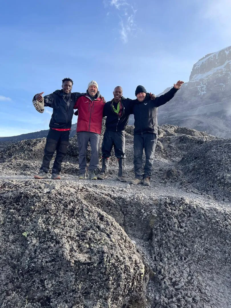 Four climbers with arms raised on the rocky upper slopes of Kilimanjaro