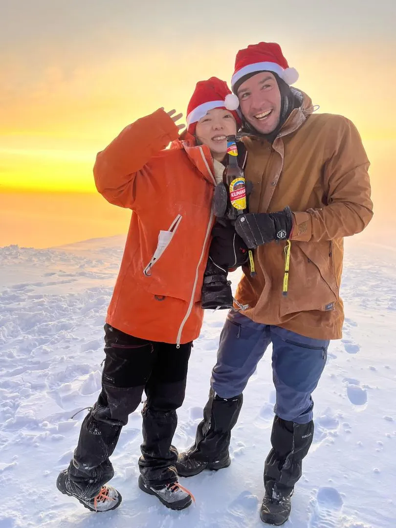 Two climbers toasting at sunrise on the snowy summit of Kilimanjaro